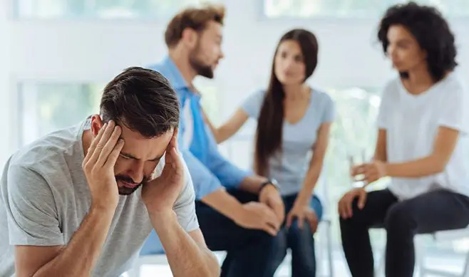 A group of people sitting in a room with one man holding his head.