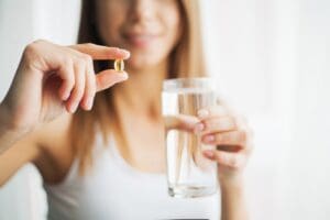 Woman holding a methadone pill and a glass of water, during long term methadone therapy