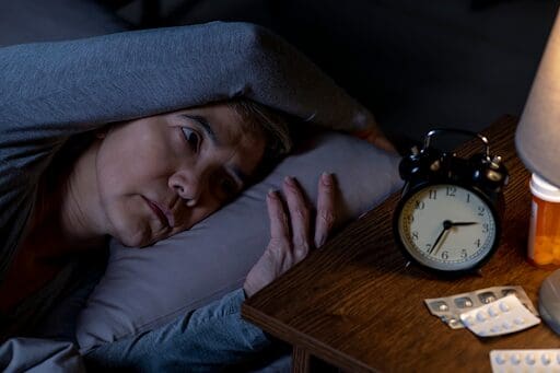 Woman in bed struggling to sleep as may happen when navigating the opioid withdrawal timeline. 