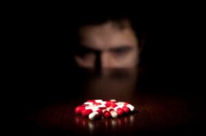 Man stares at red and white drug pills, as he deals with a craving in recovery.