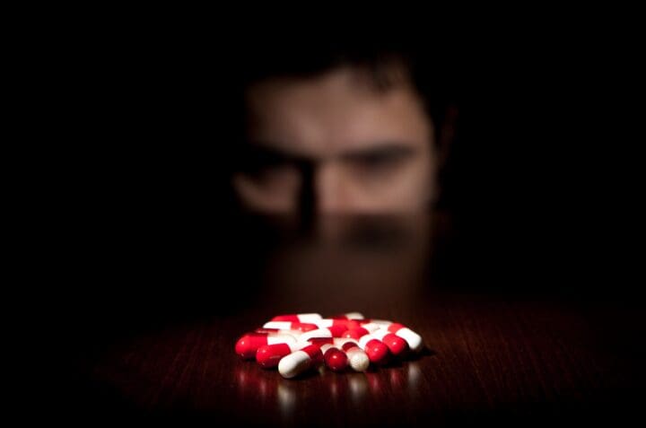 Man stares at red and white drug pills, as he deals with a craving in recovery.