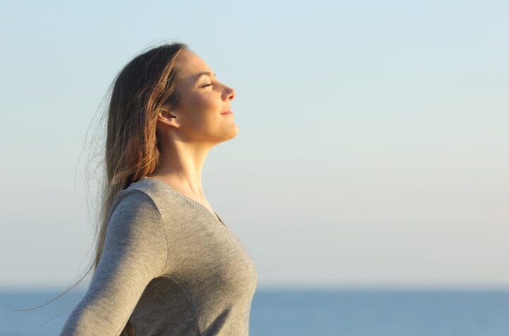 A woman breathes deeply with her arms outstretched, a great strategy when resisting a drug craving